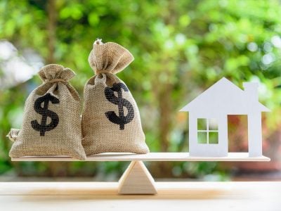 Home loan / reverse mortgage or transforming assets into cash concept : House paper model , US dollar hessian bags on a wood balance scale, depicts a homeowner or a borrower turns properties into cash
