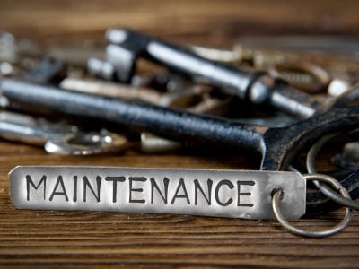 Photo of key bunch on wooden board and tag with letters imprinted on clean metal surface; concept of MAINTENANCE